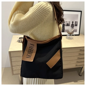 Détail du sac cabas en toile noire avec étiquette fashion marron et bandoulière