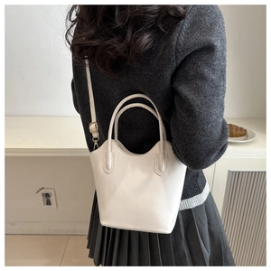 Rear view of a minimalist white bucket bag worn crossbody with elegant casual outfit
