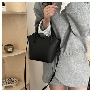 Side view of black minimalist bucket bag being held by a model for size perspective