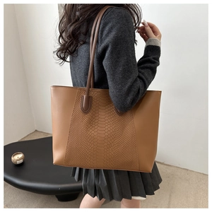 Close-up of caramel brown tote bag with crocodile texture patchwork and slim straps