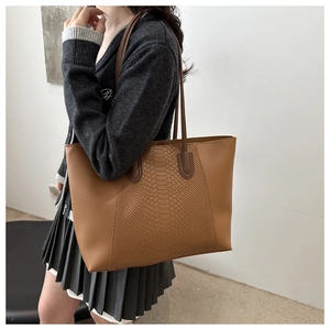Detailed view of brown tote bag with snake pattern stitching and long shoulder straps