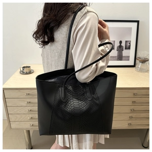 Detail of black tote bag with snake skin texture worn by a model in a minimalist room