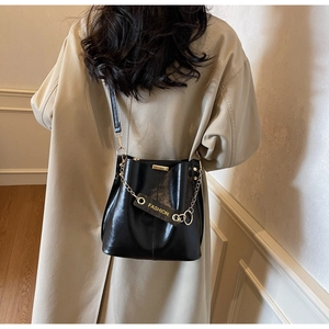Chic black leather bucket bag with fashion chain detail on a beige trench coat