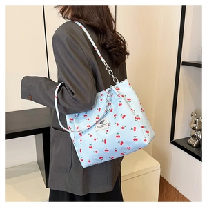 Detail of light blue cherry print tote bag with silver chain strap on model's shoulder