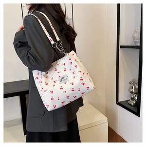 Detail of cherry print tote bag with silver metal chain strap worn by a female model