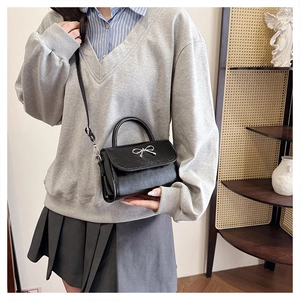 Detail of black mini crossbody bag with silver bow detail worn by model in casual style