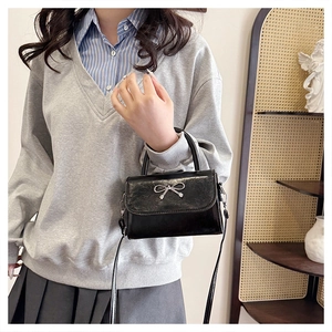 Détail d'un sac à main en cuir noir brillant avec un nœud en argent et une poignée