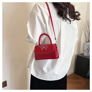 Detail of red glossy crossbody bag featuring silver bow accent and adjustable shoulder strap