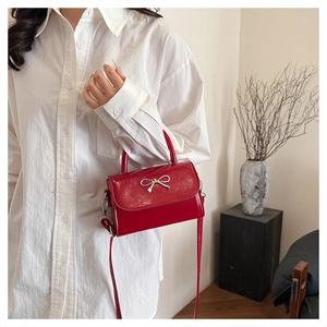 Macro detail of the silver bow buckle on a red patent leather mini crossbody handbag