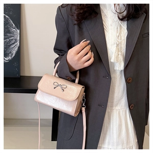 Detail of pink bow handbag with silver buckle and glossy finish shown on model