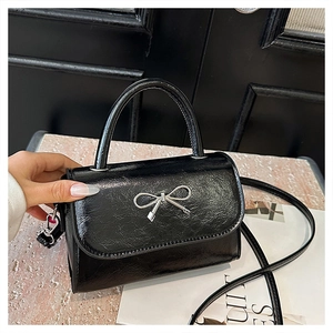 Close-up of the glossy wrinkled leather texture and silver bow detail on a black handbag