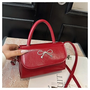 Detail of red patent leather handbag featuring a silver metal bow accent and top handle