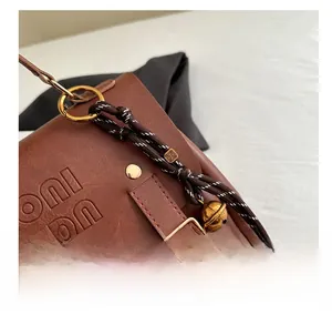 Detail view of brown PU leather bag with gold hardware, brand embossing and bag charms