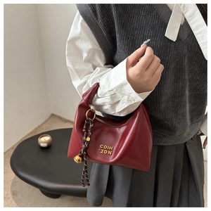 Detail of burgundy crescent bag with gold lettering and woven charm on a model