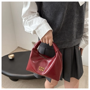 Close-up of deep red glossy crescent bag featuring a gold metal brand logo ornament