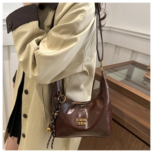 Detail of dark brown glossy leather hobo bag featuring gold logo and woven charm