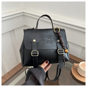 Detail of black dual-use backpack with embossed logo and gold bell charm accessory