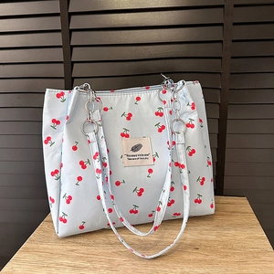 Blue cherry print tote bag with metallic chain straps shown in a lifestyle setting