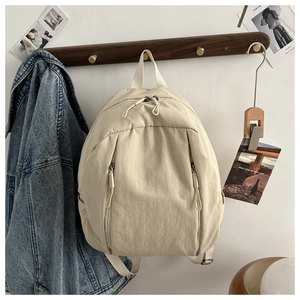 Dettaglio dello zaino in nylon beige con doppia cerniera appeso a un gancio di legno