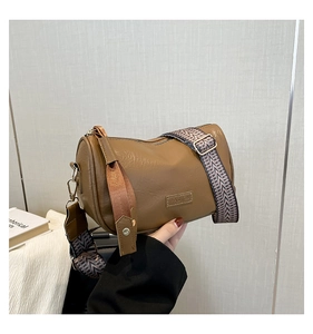 Detail of dark brown cylindrical bag with wide colorful jacquard strap and metal logo