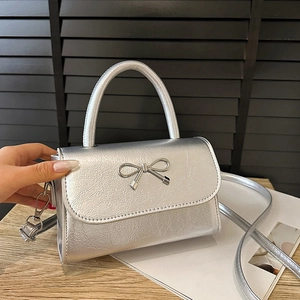 Elegant silver square crossbody bag with metallic bow and rounded handle on a wooden desk
