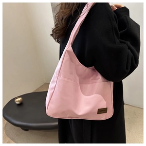 Dettaglio di una borsa tote in nylon rosa con tasca esterna e toppa in pelle griffata