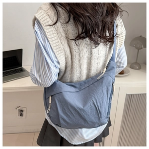 Close-up of a blue nylon half-moon crossbody bag featuring contrast white zipper pulls