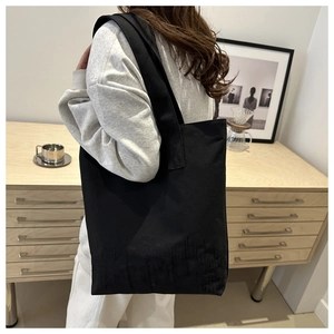 Détail du sac cabas en toile noire minimaliste avec lettrage texturé et longues bandoulières