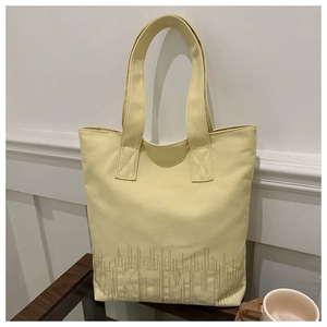 Detail of embroidered pattern and sturdy double handles on a light yellow canvas tote bag