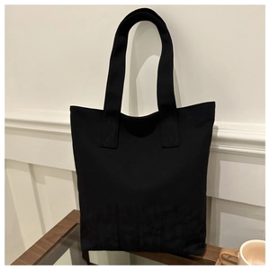 Détail d'un grand sac cabas en toile noire posé sur une table en bois décor épuré