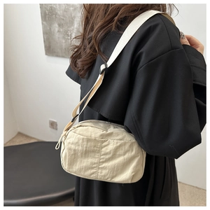 Detail of a beige nylon crossbody bag featuring adjustable strap and soft texture on model
