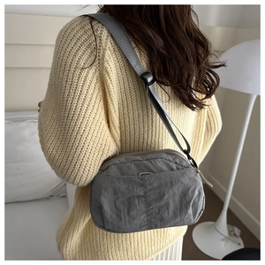 Detail view of lightweight gray nylon crossbody bag with adjustable strap on model