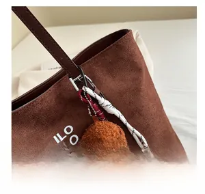 Detail of dark brown suede tote bag with white text and cute teddy dog plush pendant