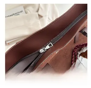 Close-up of smooth silver zipper on a brown suede tote bag with grey fabric lining