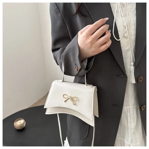 Détail du petit sac blanc en cuir avec boucle nœud doré et découpe courbe élégante