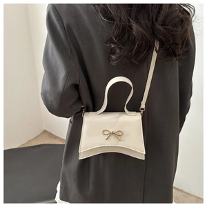 Detail of cream white mini crossbody bag with gold bow clasp and curved bottom edge
