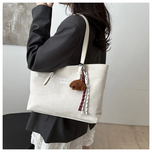 Detail of off-white suede tote bag with teddy bear charm and logo print on model