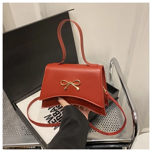 Détail du sac bandoulière en cuir rouge avec nœud doré et base incurvée élégante