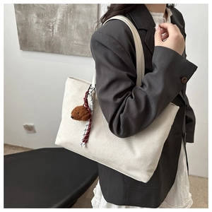 Detail of white large tote bag with a cute brown bear charm on a female shoulder
