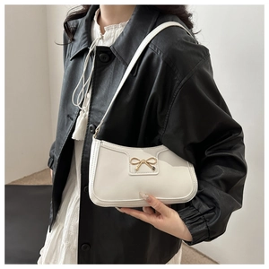 Close-up of white crescent underarm bag with gold metal bow and smooth vegan leather finish