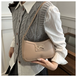Detail view of the elegant beige crescent shoulder bag with golden bow hardware