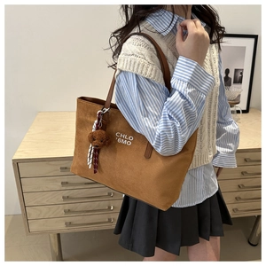 Detail of brown suede tote bag with teddy bear charm and striped strap accessory