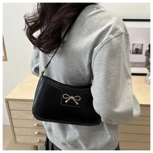 Detail of black crescent shoulder bag with golden bow buckle worn by model