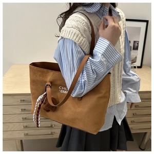 Detail of brown corduroy tote bag with letter print and plush bear charm decoration