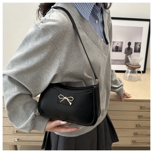 Close-up of a black leather crescent bag featuring a gold bow metallic buckle detail