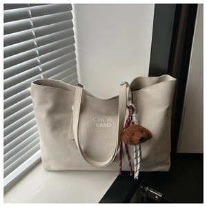 Detail of beige suede tote bag with CHLO text and cute teddy bear charm on side