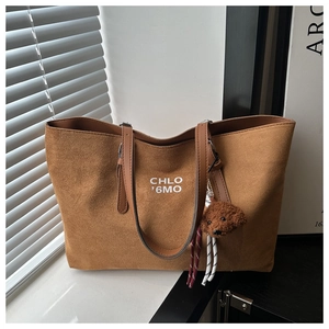 Detail of a brown corduroy tote bag featuring artistic lettering and a plush dog charm