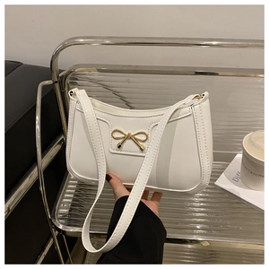 Close-up of white leather crescent underarm bag with gold bow detail and shoulder strap
