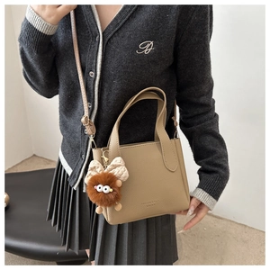 Close-up of khaki leather bucket bag with fuzzy monster charm and gold embossed logo