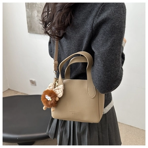 Close-up of khaki pebbled leather bucket bag featuring a plush monster charm on model